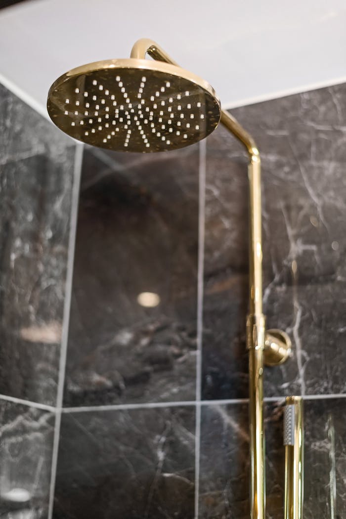Close-up of a modern gold showerhead against dark marble tiles in a designer bathroom.