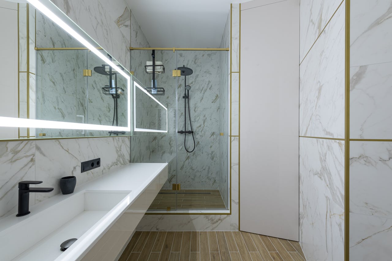 about-img Shower cabin and ceramic sink in spacious modern bathroom with marble tiled walls and big window with bright lamps